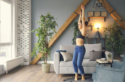 Full length of woman standing on sofa at home