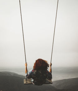 Rear view of woman swinging on rope swing against sky