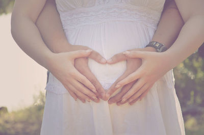 Cropped image of man with pregnant woman making heart shape on belly