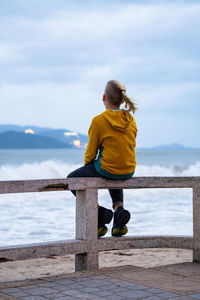 Lonely teenager looking to sea sitting on the waterfront. rear view of teenager against seascape.