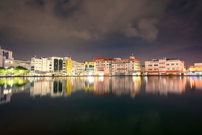 Illuminated buildings by lake against sky in city at night