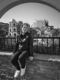 Portrait of woman sitting on railing in city