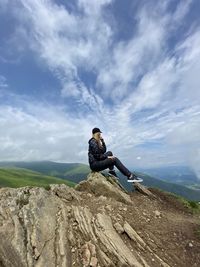 Full length of woman sitting on rock against sky