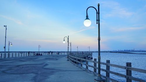 Street lights on pier by sea against sky during sunset