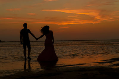 Silhouette people on beach against sky during sunset