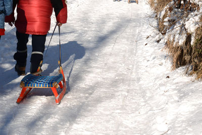 Low section of people with sledge walking on snow