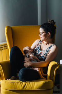 Woman sitting on yellow sofa at home holding her new born baby