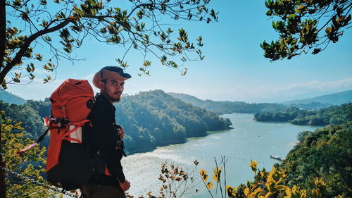 Young man standing by lake against sky