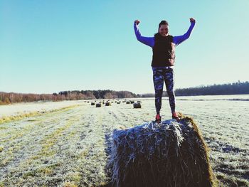 Portrait of young woman standing on hay bale against clear sky