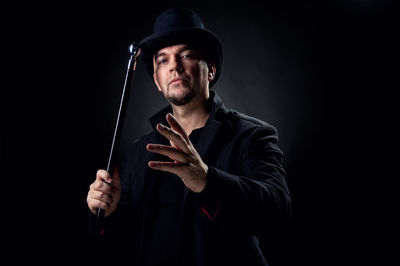 Portrait of mature man wearing hat while standing against black background