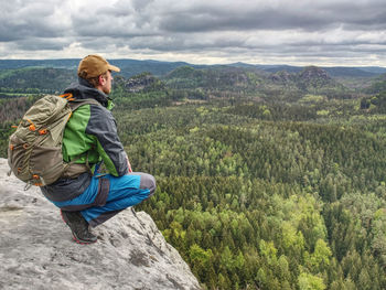 Man tourist in nature. spring free day in rocky mountains. hiker with sporty backpack stand on rock