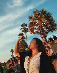 Young woman standing by palm tree against sky