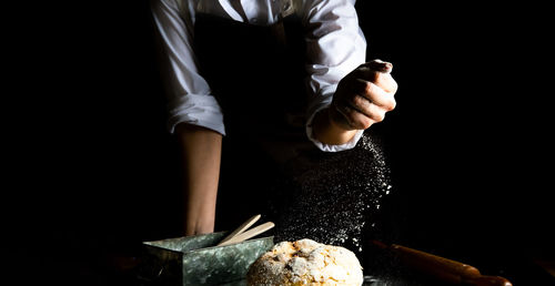 Fresh bread and chef hands with falling flour on black background. close-up