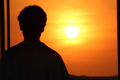 Rear view of silhouette man standing against orange sunset sky