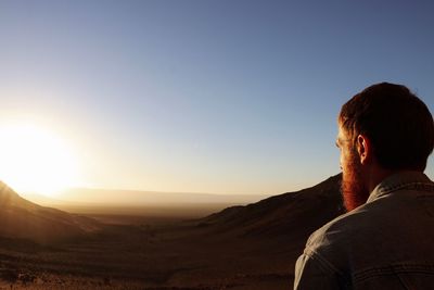 Rear view of man looking at mountains against sky