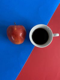 Directly above shot of coffee and apple on red and blue background