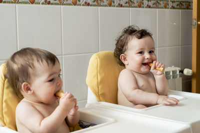 Laughing baby child eating bread sticks with his twin sister.