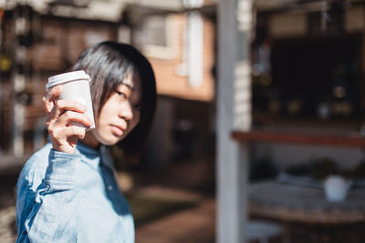 Portrait of mid adult woman showing disposable cup while standing in cafe