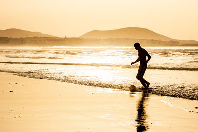 Silhouette man on beach against sky during sunset