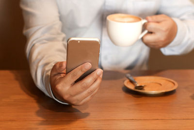 Midsection of man holding coffee cup on table