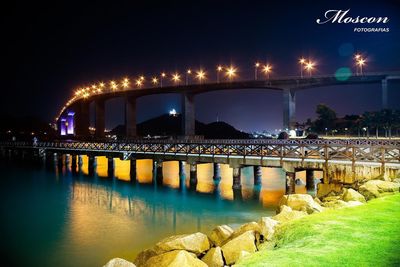 Illuminated bridge over river in city at night