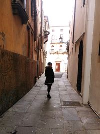 Rear view of man walking on footpath amidst buildings