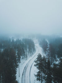 Snow covered road by trees against sky