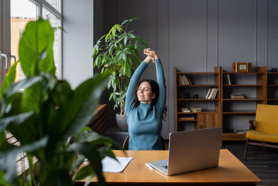 Relaxed female stretching hands taking break from work on laptop look in window in coworking space
