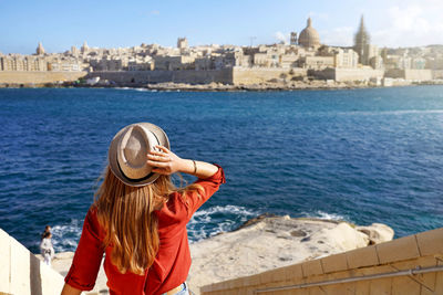 Woman with hat descends stairs in malta looking at panoramic view of valletta, malta