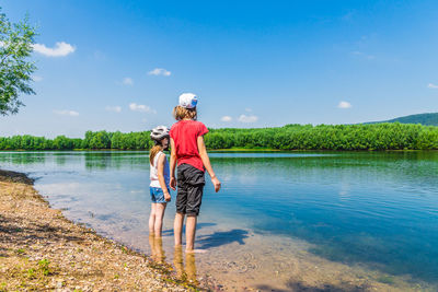 Rear view of friends standing on lake against blue sky