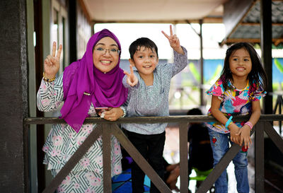Portrait of smiling mother and children standing against railing