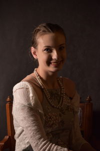 Portrait of smiling young woman sitting against black background