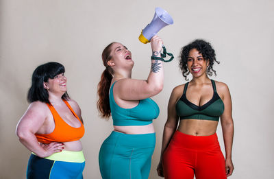 Smiling friends holding megaphone against colored background