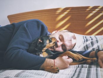 Man kissing dog while lying on bed at home