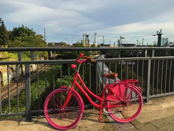 Bicycle parked by railing bridge against sky in city