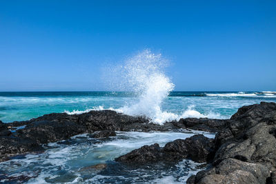 Sea waves splashing on rocks against blue sky