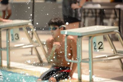 Drops in mid-air against teenage boy sitting at poolside by diving platform