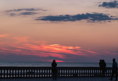 Silhouette people looking at sea against sky during sunset