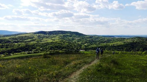 Rear view of hikers on grassy field against sky