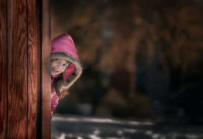 Portrait of girl smiling while standing behind wooden wall during winter