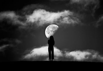 Silhouette woman standing on field against moon in sky