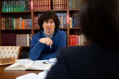 Portrait of man with pencil holding by nose and lips at library