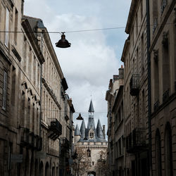 Low angle view of lighting equipment hanging amidst buildings against sky