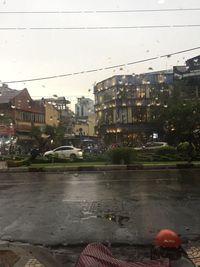 Wet street amidst buildings against sky during rainy season