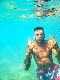 Portrait of shirtless man gesturing while swimming in sea