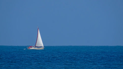 Sailboat sailing in sea against clear blue sky