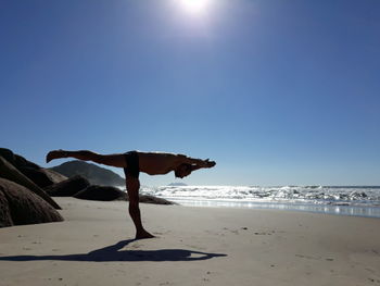 Full length of man doing yoga at beach on sunny day