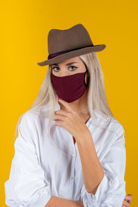 Portrait of woman wearing mask and hat against yellow background