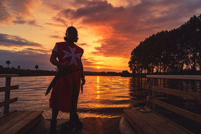 Man standing by lake against sky during sunset