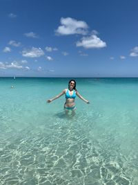 Portrait of woman wearing bikini while standing in sea against blue sky